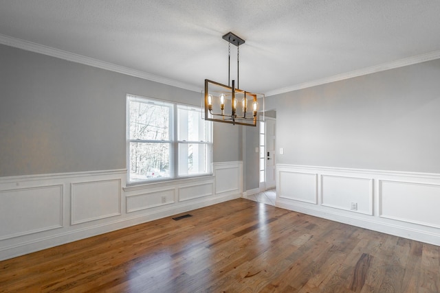 unfurnished dining area featuring hardwood / wood-style floors, a textured ceiling, crown molding, and a chandelier