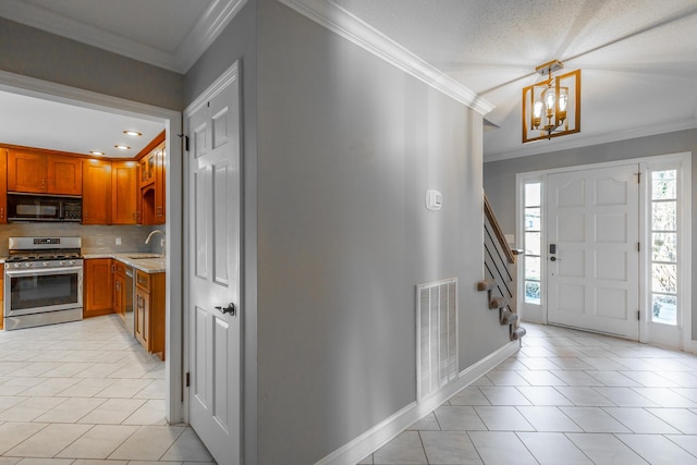 tiled foyer entrance with a textured ceiling, sink, crown molding, and an inviting chandelier