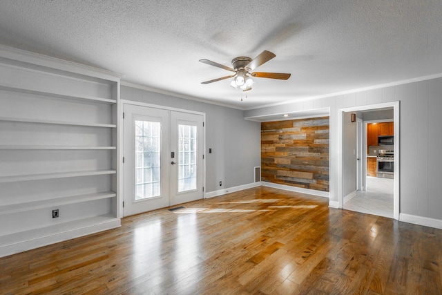 unfurnished room with french doors, ceiling fan, wooden walls, crown molding, and built in features