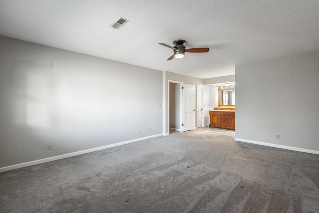 unfurnished bedroom featuring ensuite bathroom, ceiling fan, a textured ceiling, and dark colored carpet