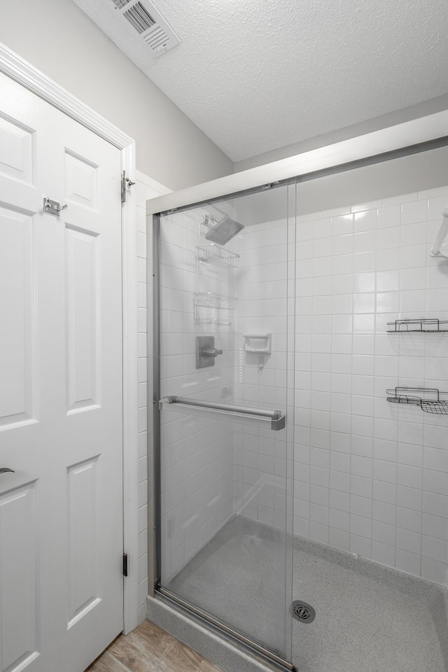 bathroom with a shower with door, wood-type flooring, and a textured ceiling