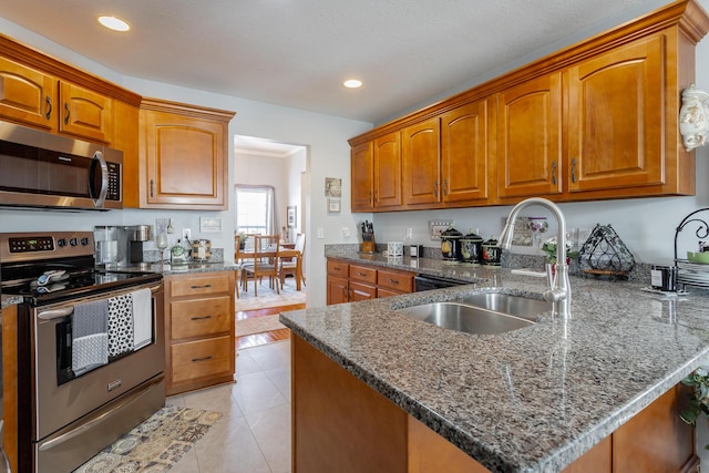 kitchen featuring sink, light tile patterned floors, kitchen peninsula, dark stone counters, and appliances with stainless steel finishes