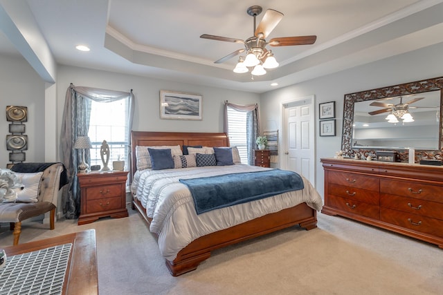 carpeted bedroom with a raised ceiling, ceiling fan, multiple windows, and ornamental molding