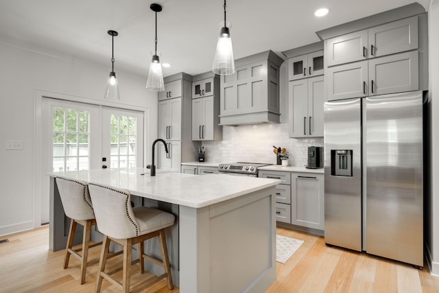 kitchen featuring sink, premium range hood, decorative light fixtures, a kitchen island with sink, and appliances with stainless steel finishes