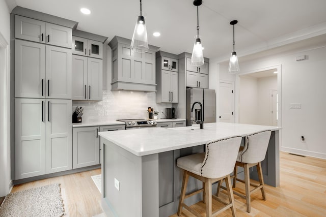 kitchen featuring decorative light fixtures, gray cabinets, an island with sink, and appliances with stainless steel finishes