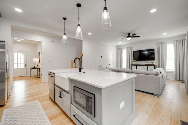 kitchen featuring a center island with sink, light hardwood / wood-style flooring, decorative light fixtures, and appliances with stainless steel finishes