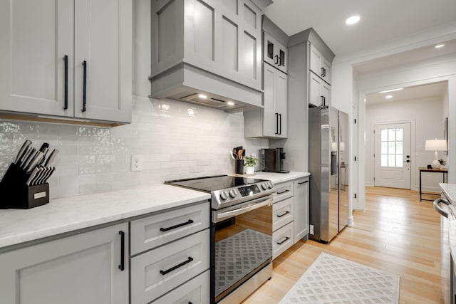 kitchen with tasteful backsplash, light stone counters, light hardwood / wood-style floors, stainless steel appliances, and gray cabinets