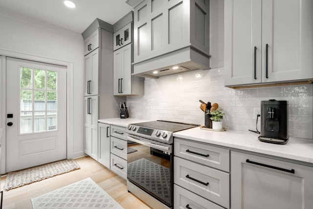 kitchen featuring light stone counters, light hardwood / wood-style flooring, backsplash, premium range hood, and stainless steel range with electric stovetop