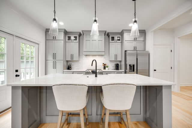 kitchen with gray cabinetry, stainless steel fridge with ice dispenser, hanging light fixtures, and a large island with sink