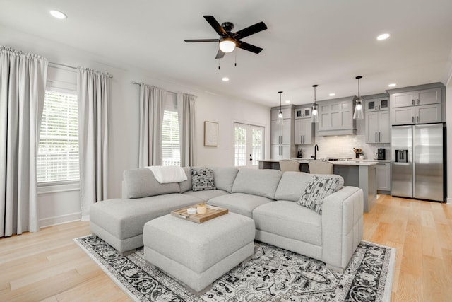 living room with ceiling fan, light hardwood / wood-style flooring, french doors, and sink