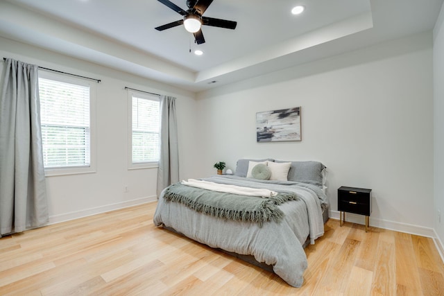 bedroom with light wood-type flooring, a raised ceiling, and ceiling fan