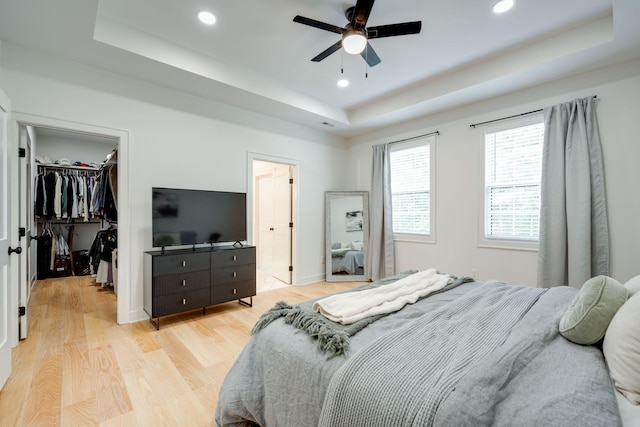 bedroom featuring light wood-type flooring, a tray ceiling, a spacious closet, and ceiling fan