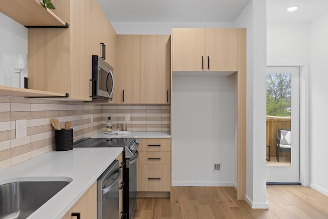 kitchen with light brown cabinets, backsplash, appliances with stainless steel finishes, and light hardwood / wood-style flooring