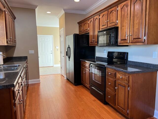 kitchen with black appliances, light wood-type flooring, ornamental molding, and sink