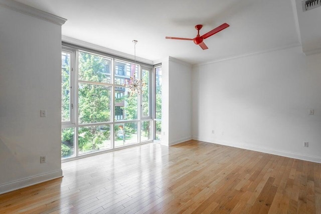 unfurnished room featuring ceiling fan, expansive windows, light wood-type flooring, and crown molding