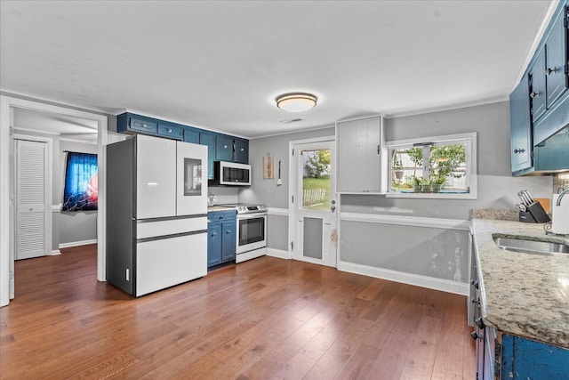 kitchen with electric range, sink, light stone counters, blue cabinets, and white refrigerator