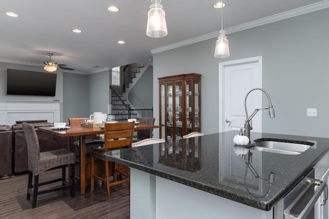 kitchen featuring ceiling fan, sink, hanging light fixtures, dark stone countertops, and a center island with sink