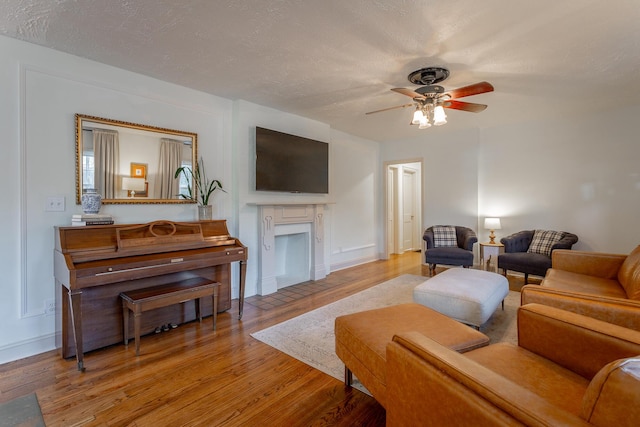 living room featuring ceiling fan, light hardwood / wood-style flooring, and a textured ceiling