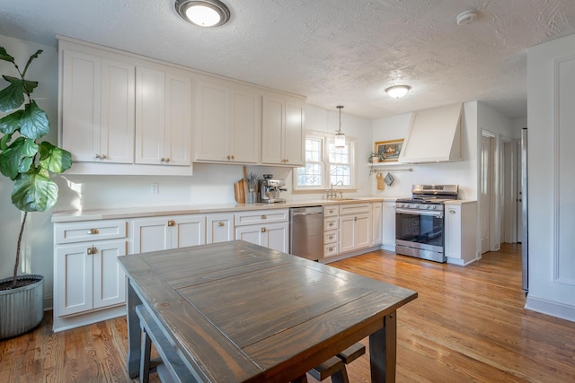 kitchen with pendant lighting, custom exhaust hood, white cabinetry, and appliances with stainless steel finishes