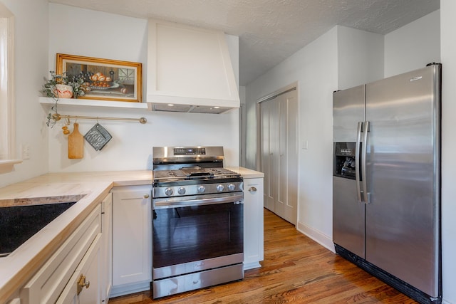 kitchen with appliances with stainless steel finishes, custom exhaust hood, a textured ceiling, light hardwood / wood-style floors, and white cabinetry