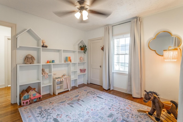 recreation room with ceiling fan, wood-type flooring, and a textured ceiling