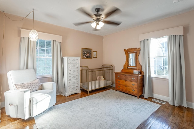 bedroom featuring hardwood / wood-style floors, a nursery area, and ceiling fan