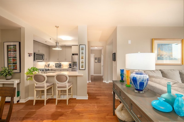 kitchen featuring sink, light hardwood / wood-style floors, a breakfast bar area, pendant lighting, and appliances with stainless steel finishes