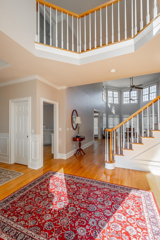 entrance foyer featuring wood-type flooring, a towering ceiling, ceiling fan, and crown molding