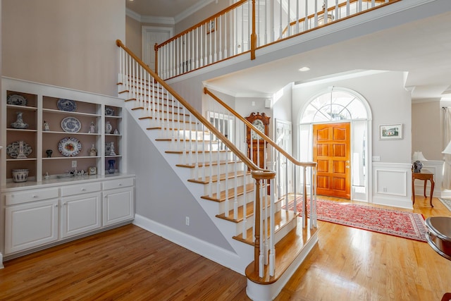 foyer entrance featuring wood-type flooring, a towering ceiling, and crown molding