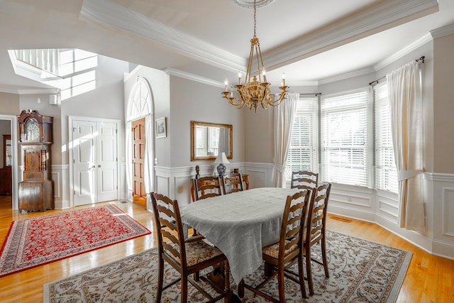 dining room featuring a raised ceiling, light wood-type flooring, ornamental molding, and an inviting chandelier