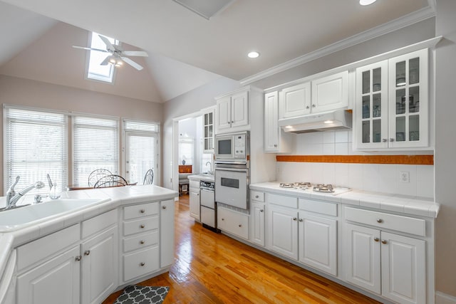 kitchen with white cabinetry, tile counters, sink, decorative backsplash, and vaulted ceiling with skylight