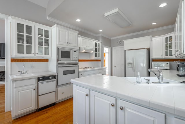 kitchen with white appliances, sink, tile countertops, light hardwood / wood-style flooring, and white cabinets