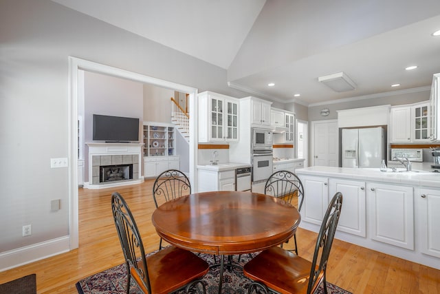 dining space with sink, light hardwood / wood-style flooring, lofted ceiling, and a tiled fireplace