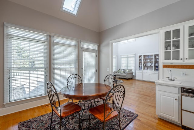 dining room with a healthy amount of sunlight, light wood-type flooring, sink, and lofted ceiling with skylight