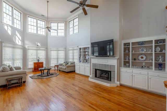 living room featuring ceiling fan, a fireplace, a high ceiling, and light hardwood / wood-style flooring