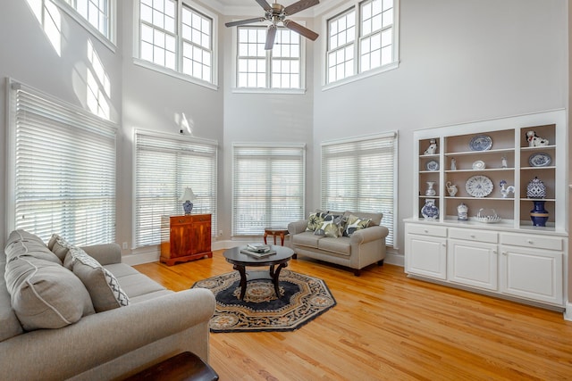 living room with ceiling fan, light hardwood / wood-style flooring, and a towering ceiling