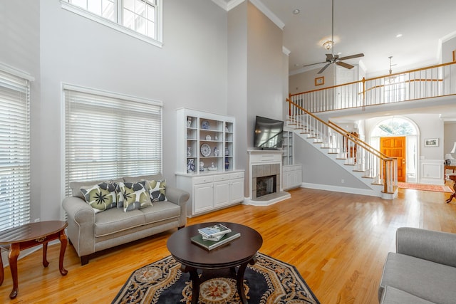 living room with light wood-type flooring, crown molding, a high ceiling, and a tiled fireplace