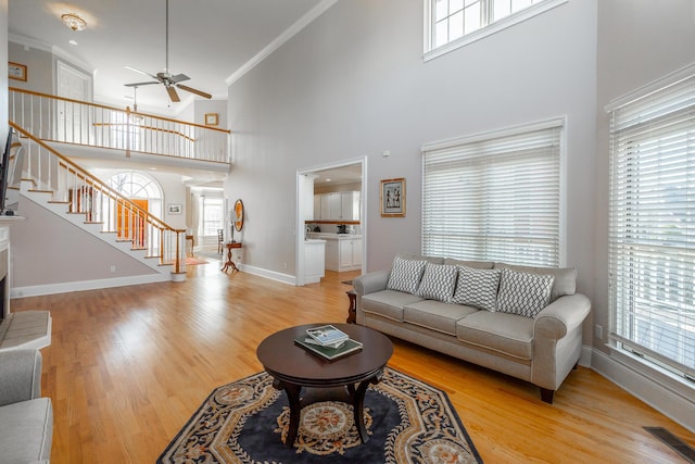 living room with crown molding, ceiling fan, light hardwood / wood-style floors, and a high ceiling