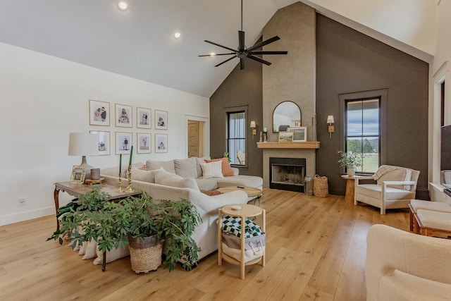 living room featuring a large fireplace, high vaulted ceiling, light hardwood / wood-style flooring, and ceiling fan