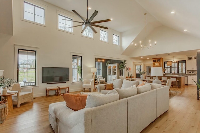 living room with ceiling fan with notable chandelier, light wood-type flooring, and a towering ceiling