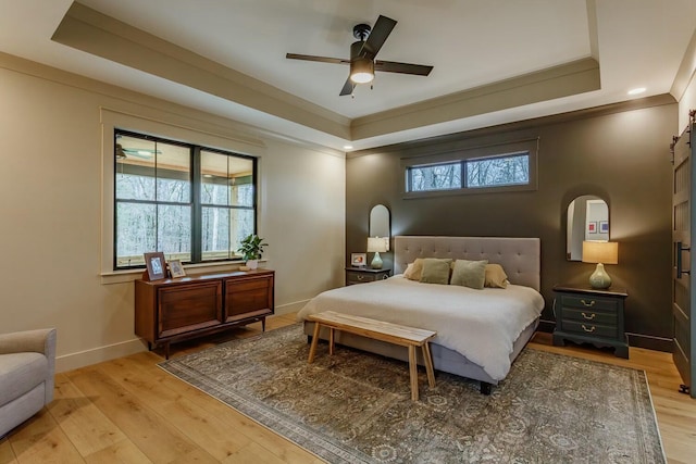 bedroom featuring light wood-type flooring, a raised ceiling, and ceiling fan