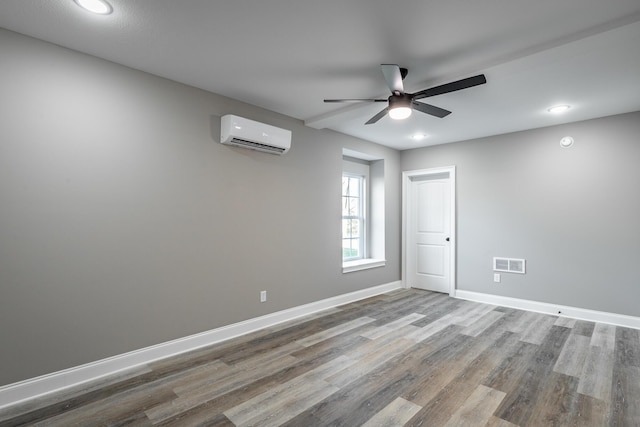 empty room with a wall unit AC, ceiling fan, and wood-type flooring