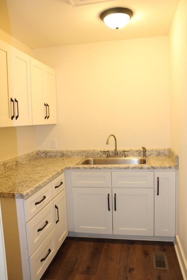 kitchen with light stone countertops, sink, white cabinets, and dark hardwood / wood-style floors