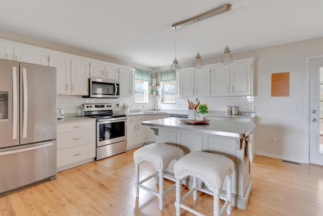 kitchen with white cabinetry, appliances with stainless steel finishes, decorative light fixtures, a kitchen island, and sink