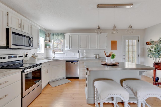 kitchen featuring stainless steel appliances, pendant lighting, white cabinets, and sink