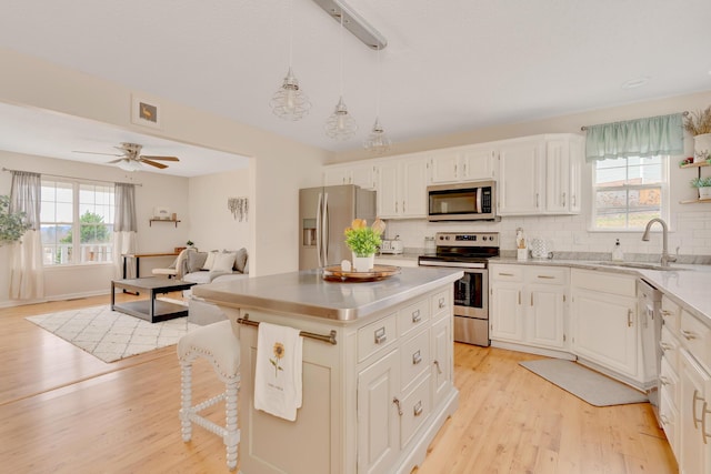 kitchen with white cabinets, appliances with stainless steel finishes, a center island, sink, and hanging light fixtures