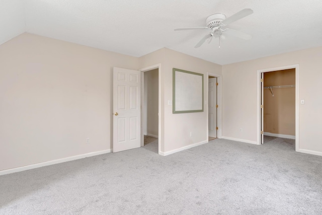 unfurnished bedroom featuring a walk in closet, light carpet, a closet, vaulted ceiling, and ceiling fan