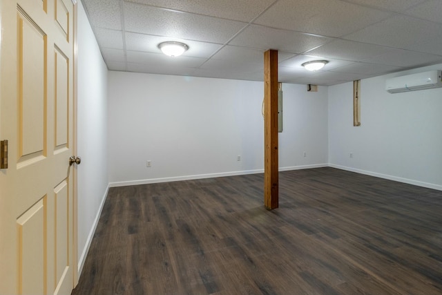 basement with a paneled ceiling, an AC wall unit, and dark wood-type flooring