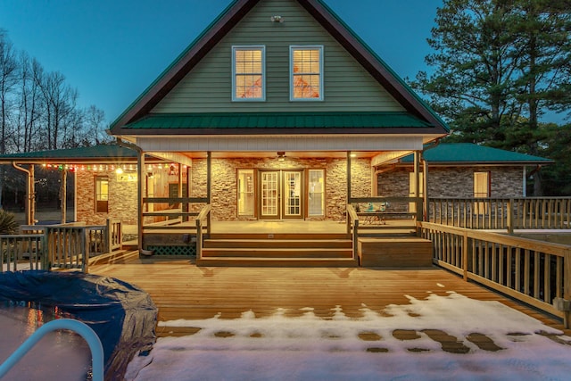 back house at dusk with a wooden deck and covered porch