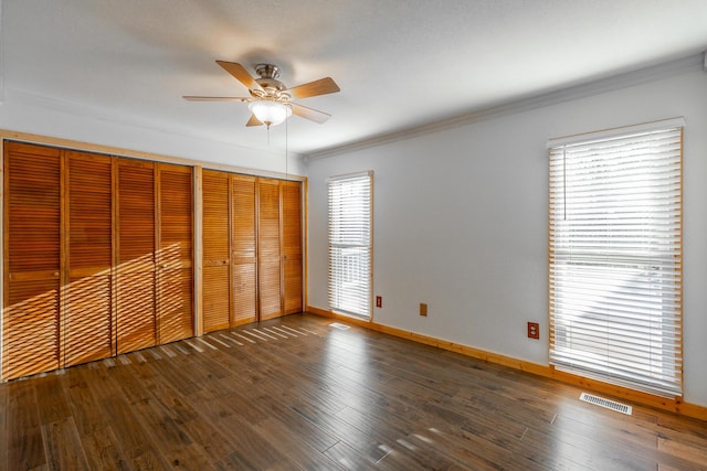 unfurnished bedroom featuring ceiling fan, two closets, multiple windows, and dark wood-type flooring